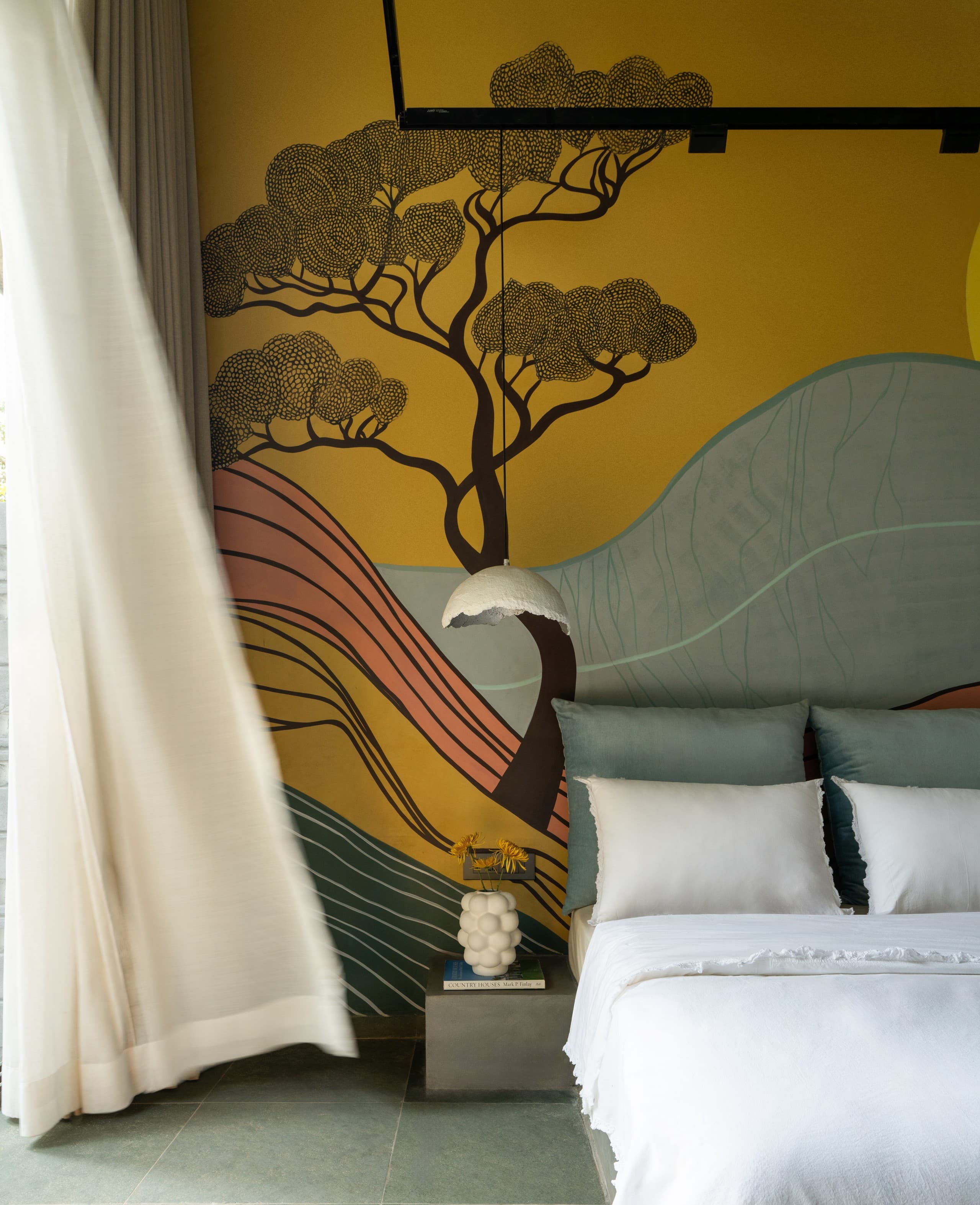 Bedroom beneath a painted-hills mural, white bedding and teal cushions.