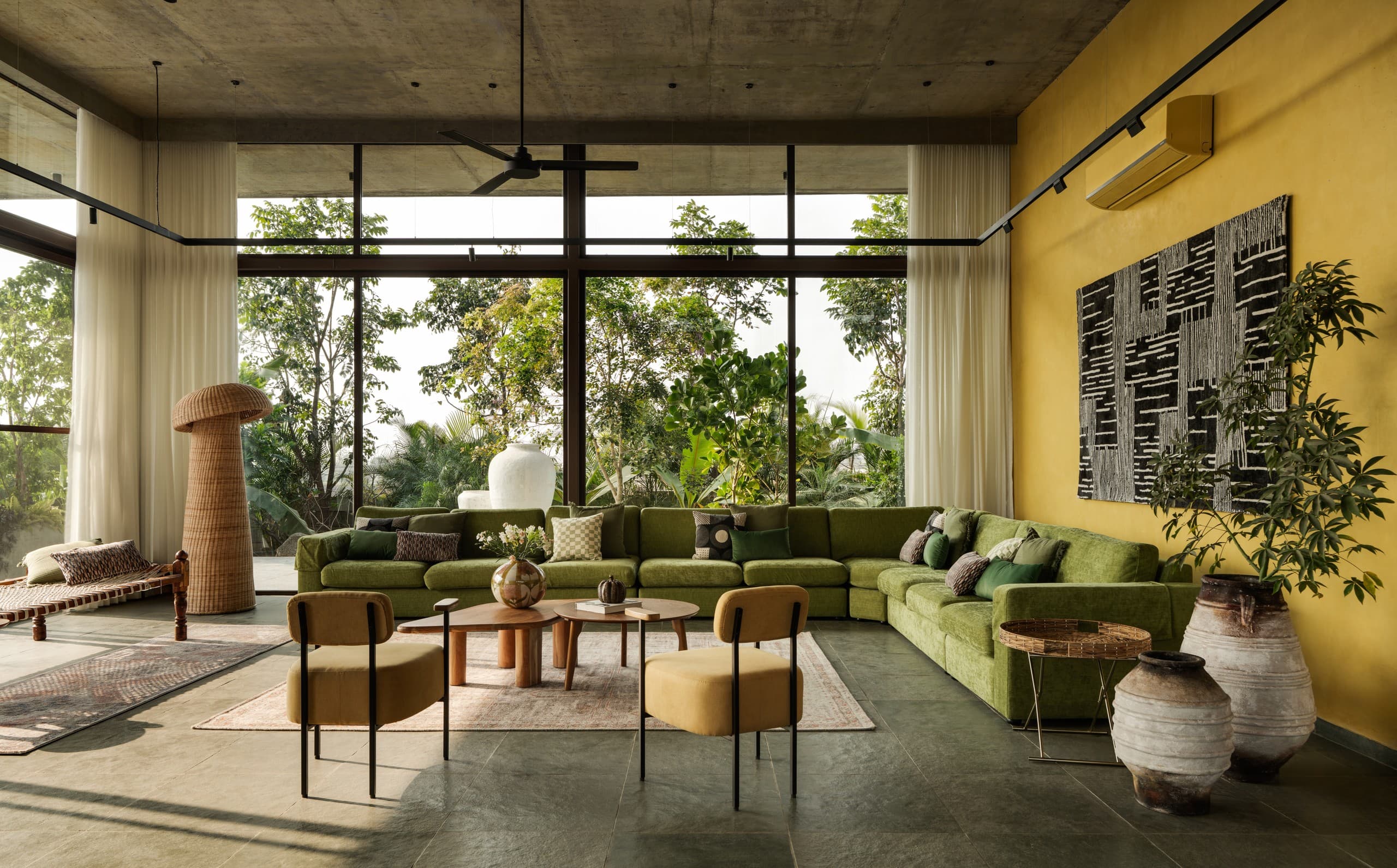 The living room open to the garden through full-height glazing, wicker lamp at left.