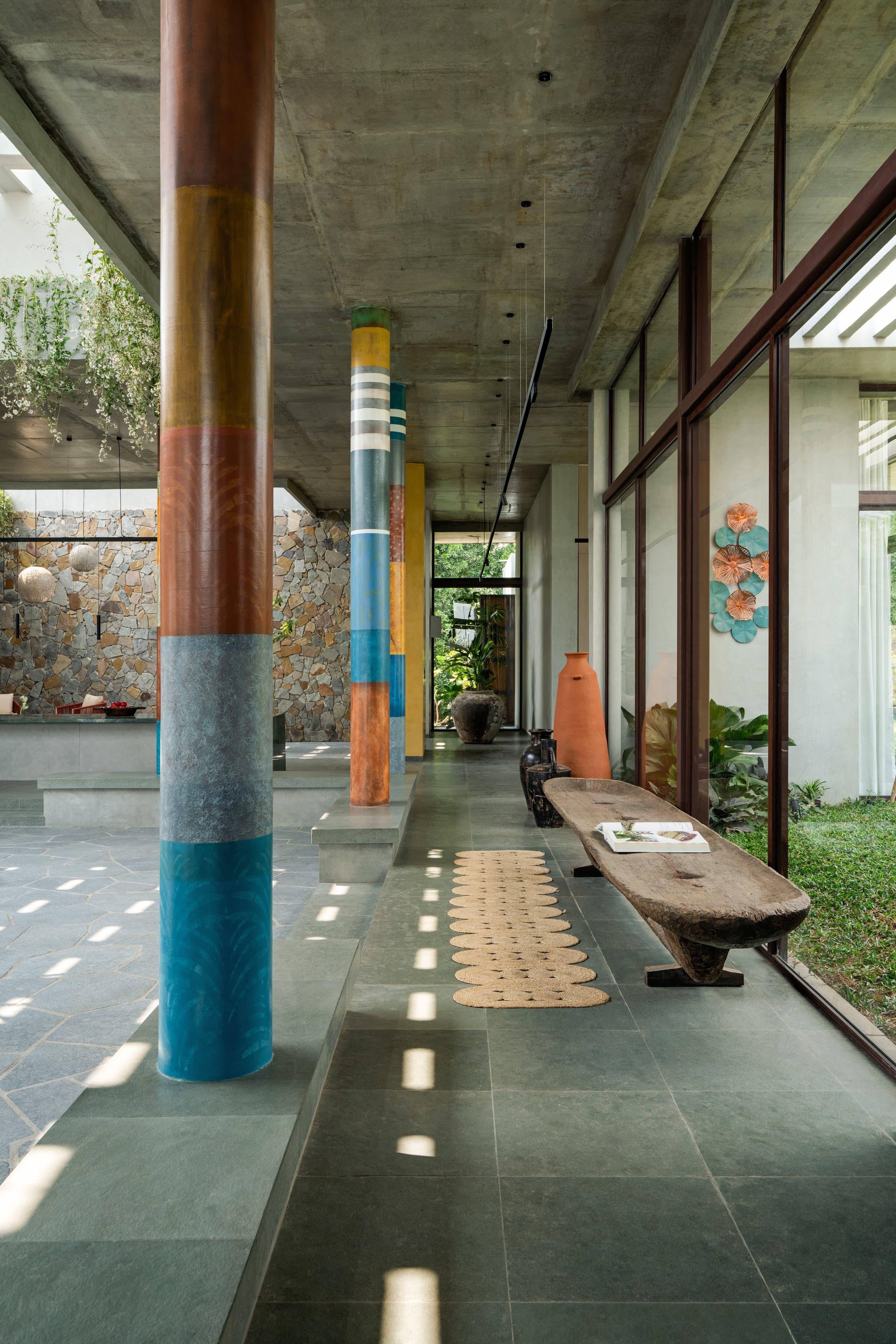 Corridor of painted columns with a carved wooden bench and terracotta vessels.