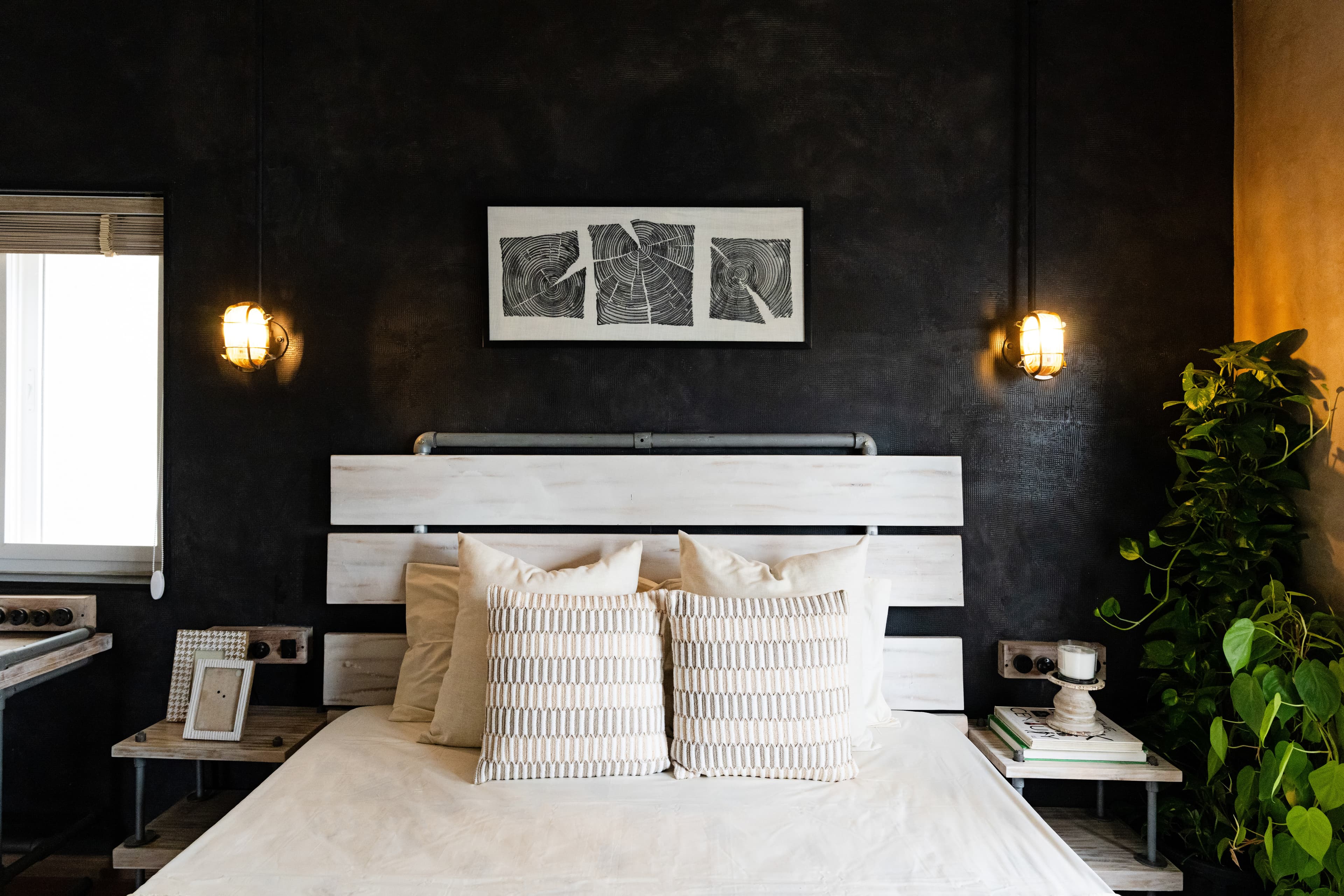 Bedroom with whitewashed plank headboard on a black wall, tree-ring woodcuts above.