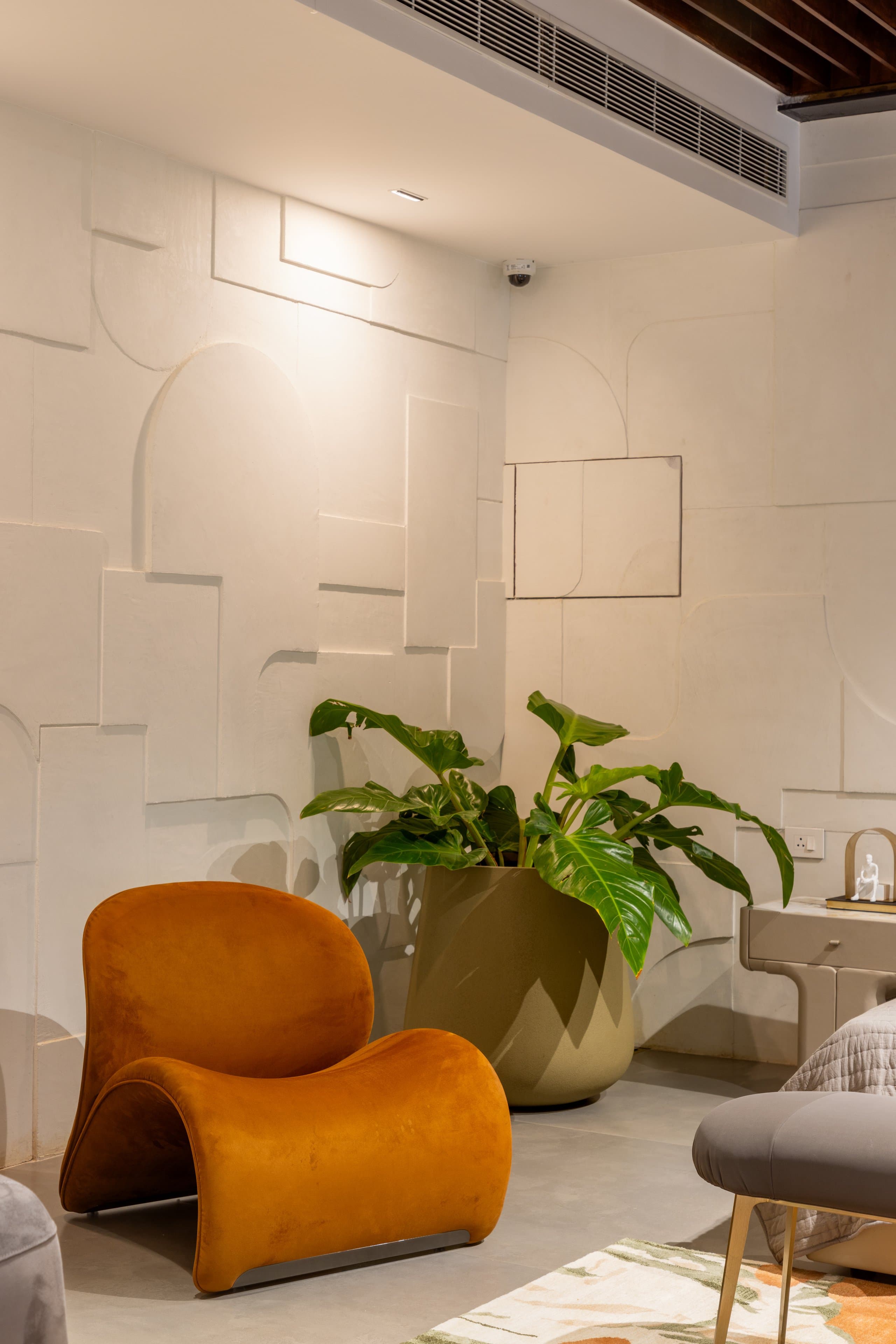 Mustard velvet armchair against a relief-plaster wall with one planter.