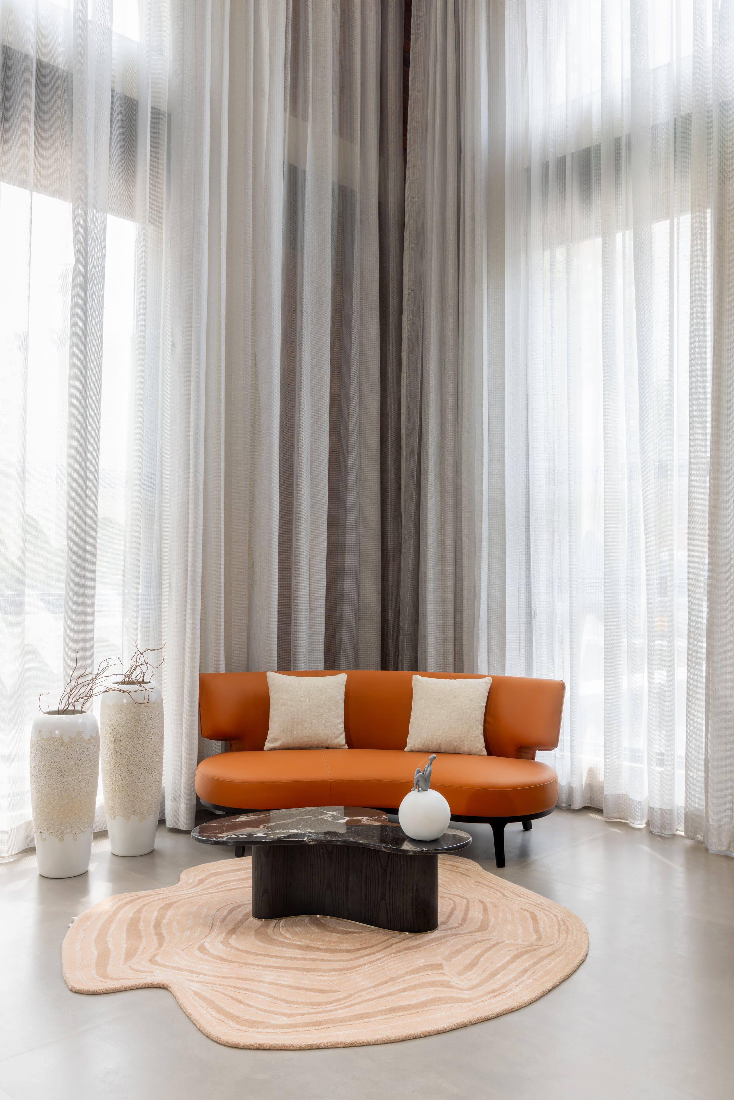 Entrance vignette: one orange loveseat, two white floor vessels, a sculpted rug and dark table.