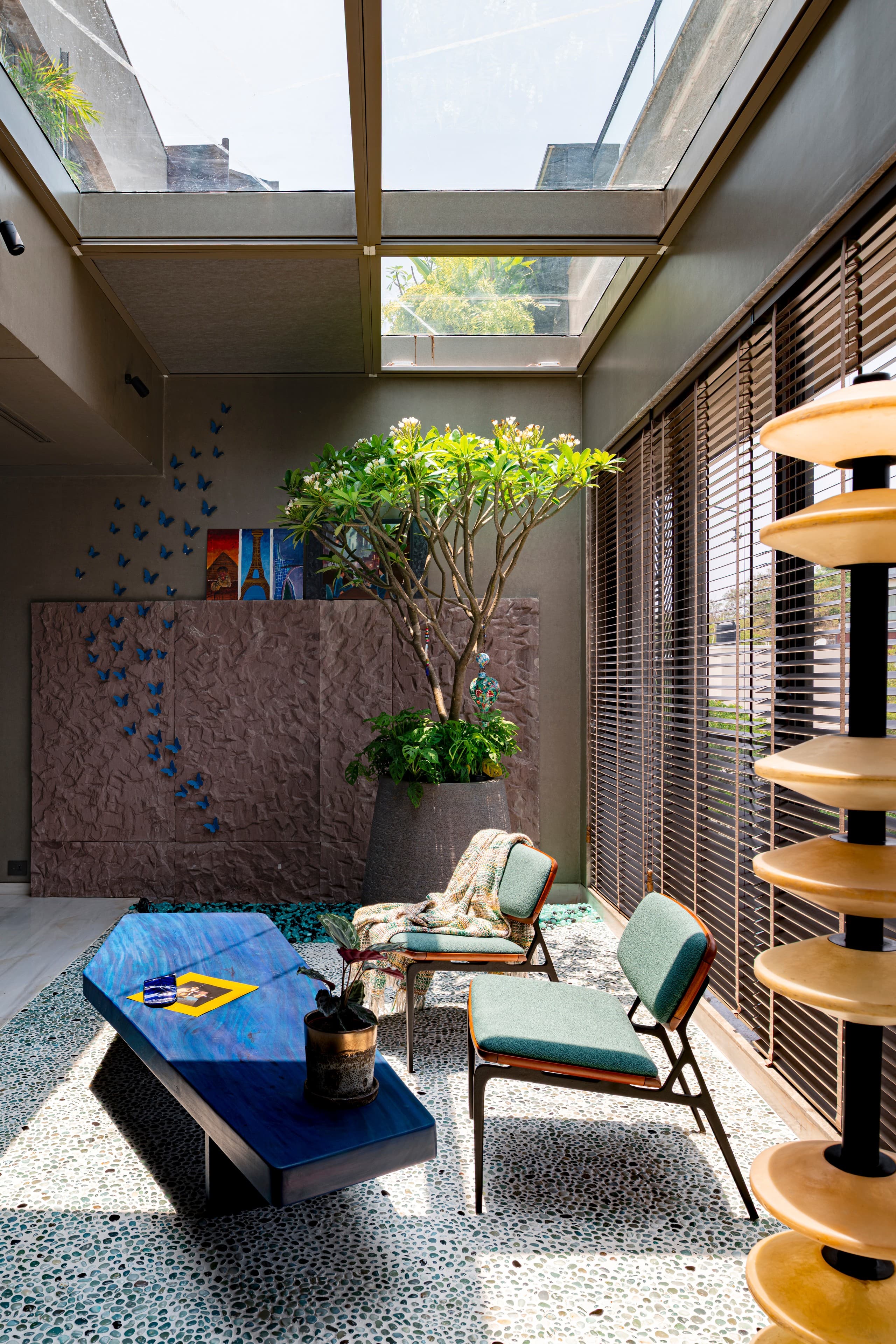 Garden room: blue resin table on a pebbled floor, ceramic butterflies climbing the wall.
